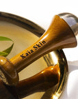 Kaia Skin Kansa Wand on a linen cloth beside face oil bottles, brass bowl, and Ayurvedic ritual setup